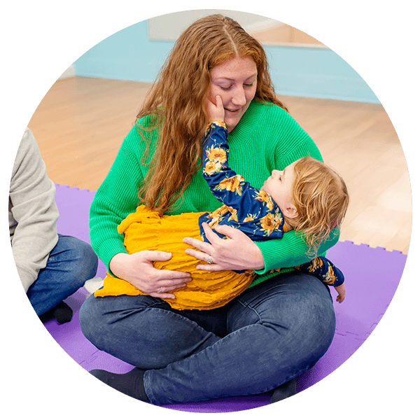 Mom singing and holding daughter in lap with child raising arm to cheek
