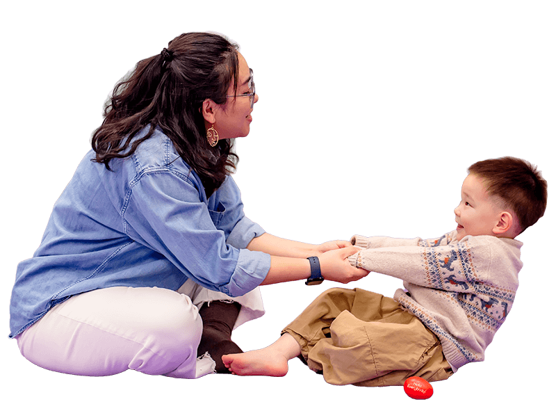 Mom and child sitting across from each other singing and holding hands in a rowing motion