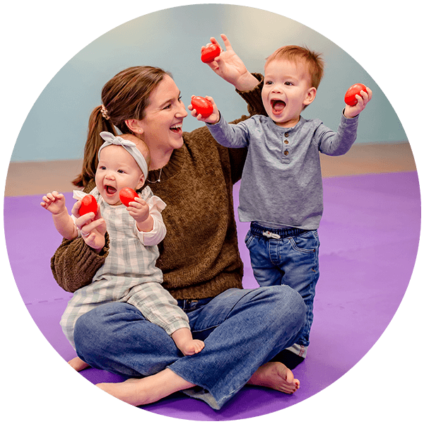 Happy mom, baby, and young child sitting on floor playing with egg shakers