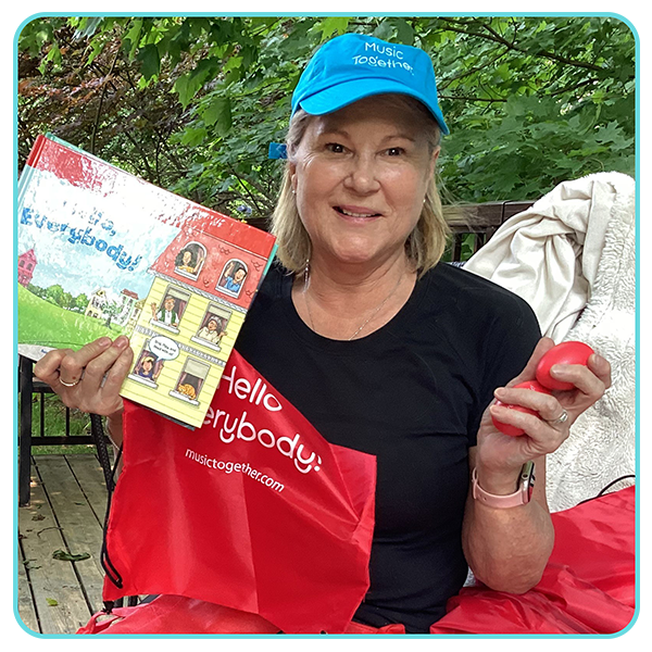 Jennifer wearing Music Together hat and holding egg shakers and Hello Everybody singalong storybook